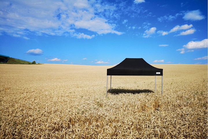 Čierny párty stan 2x3m na poli pod jasnou modrou oblohou